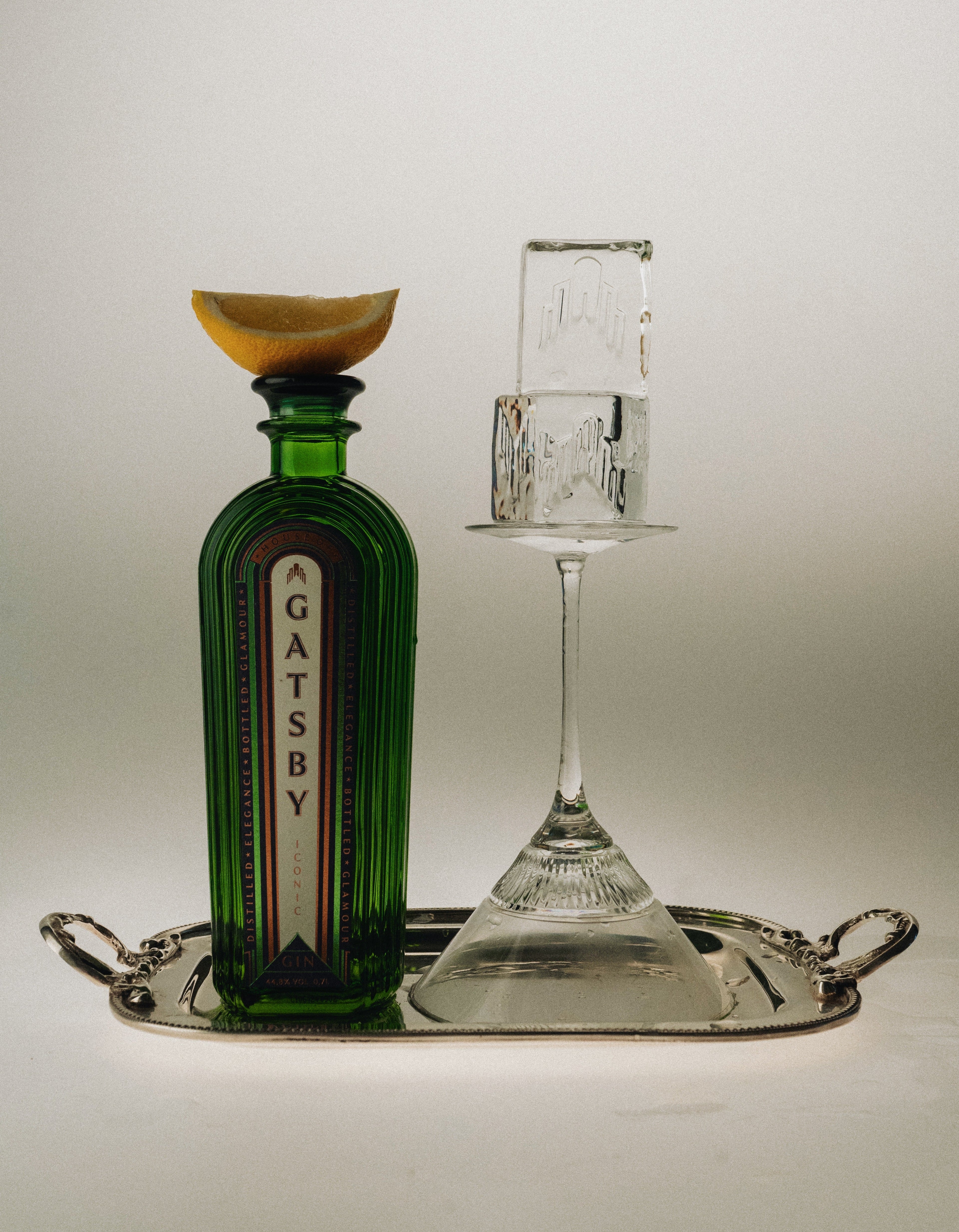 Gatsby Gin emerald bottle with lemon wedge and coupe glass on a silver tray